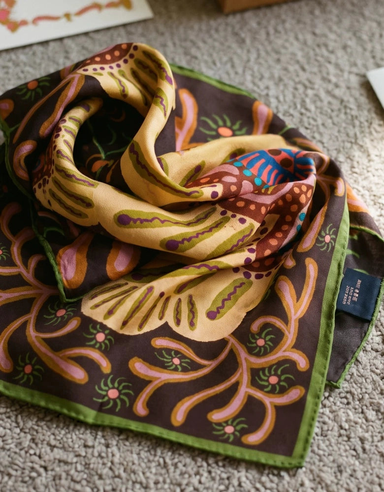 Close-up of an espresso brown silk square scarf folded to show its beige floral medallion and scrolling border