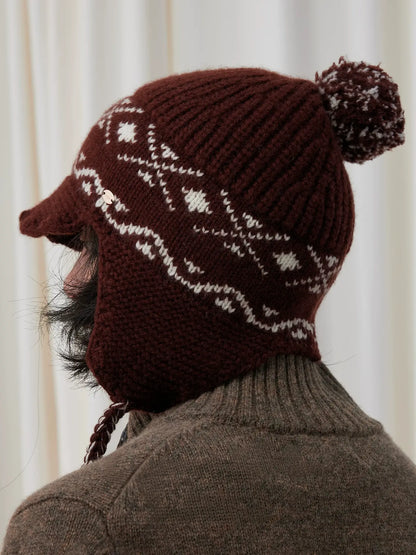 Rear three-quarter view of a coffee brown Fair Isle earflap beanie showing cream jacquard, a ribbed crown and pom pom.