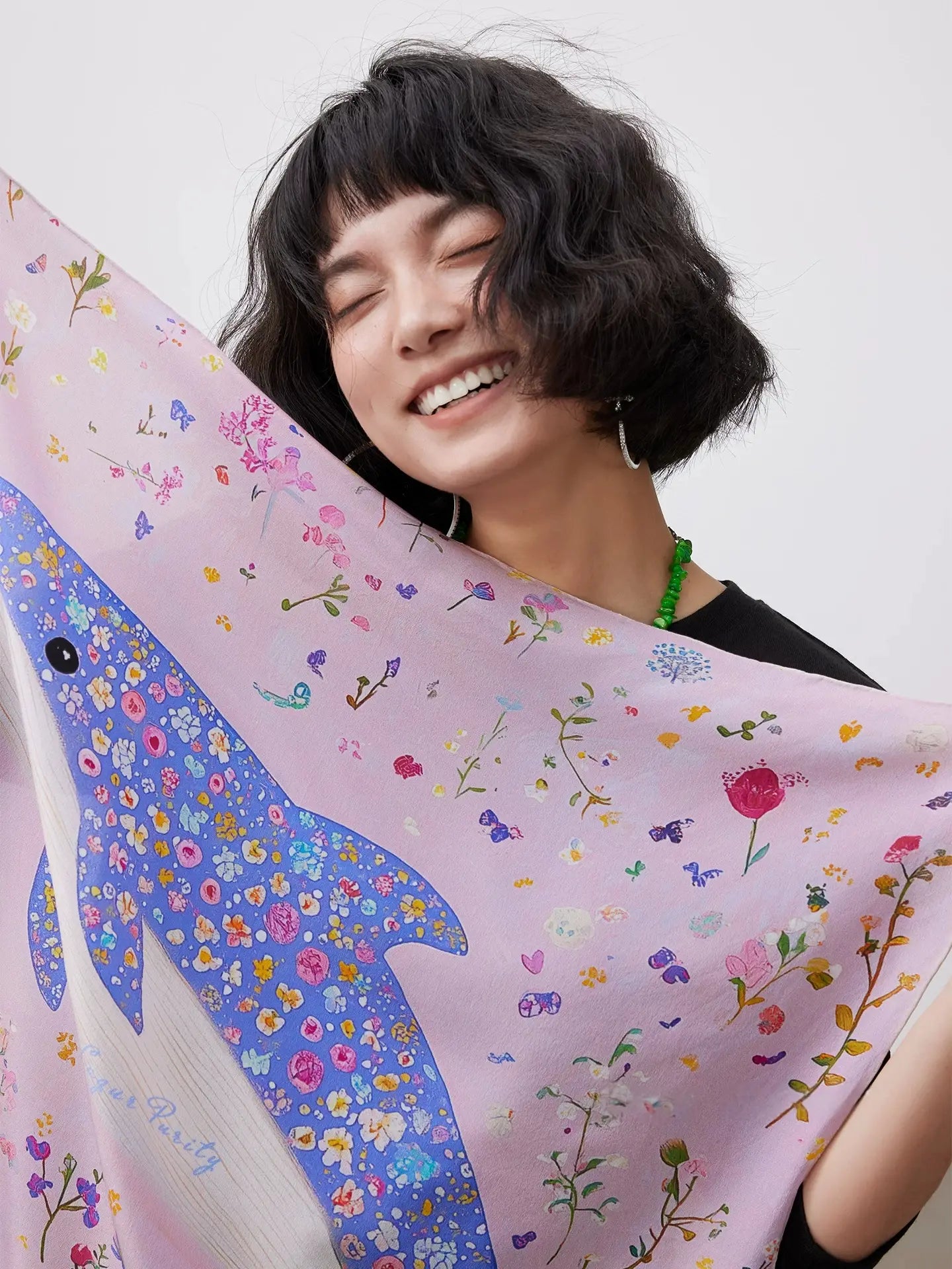 Pink silk square scarf with blue dolphin, flowers, and botanical details displayed by a model.