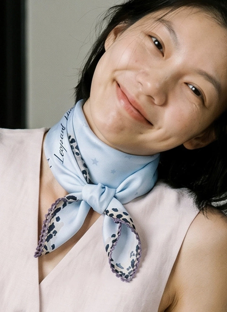 Glacier blue leopard-trim silk scarf tied at the neck in a relaxed knot