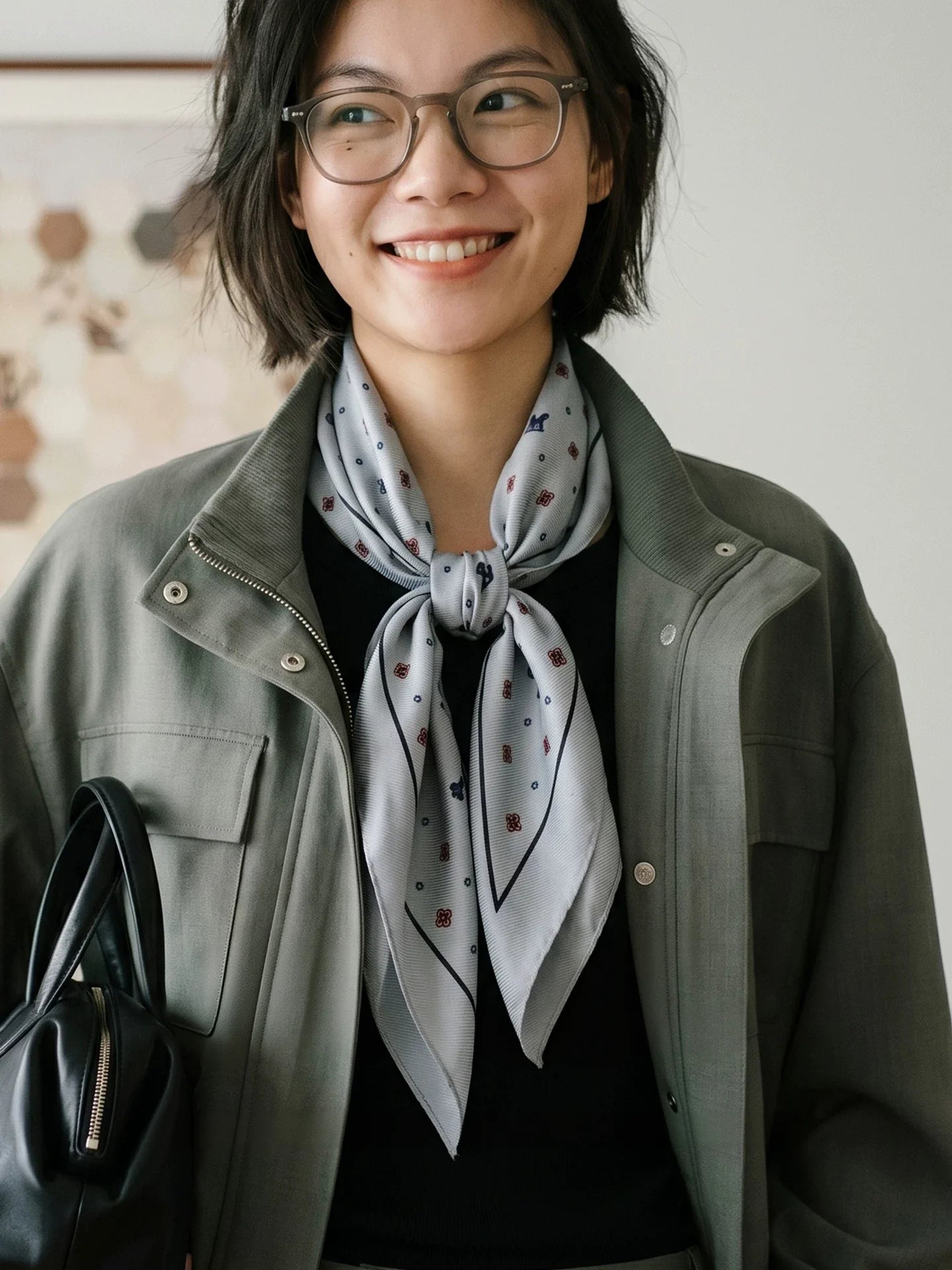 Model wearing a gray ditsy floral silk wool scarf knotted over an olive jacket