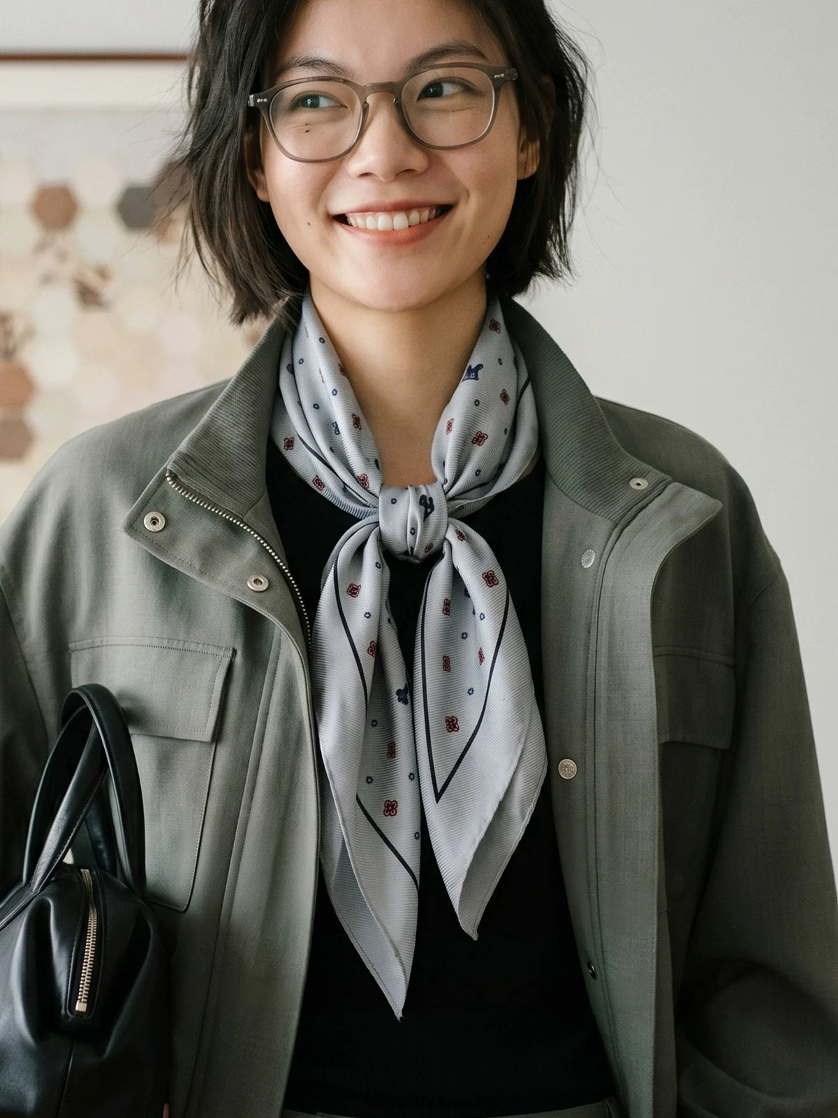 Model wearing a gray ditsy floral silk wool scarf knotted over an olive jacket