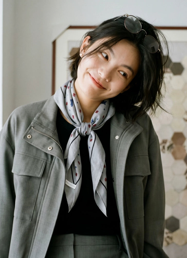 Model wearing a gray ditsy floral diamond scarf loosely wrapped with an olive jacket