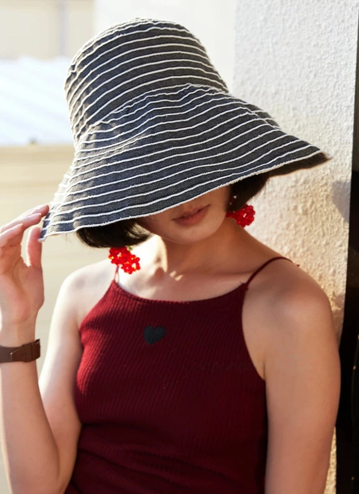 Woman adjusting a packable striped sun hat with a soft brim for comfortable outdoor shade.