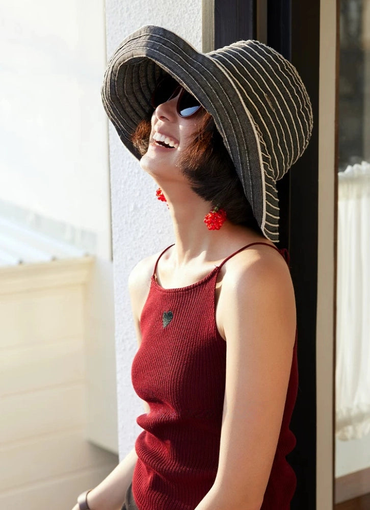 Woman wearing a gray and white foldable summer hat beside a window in natural sunlight.