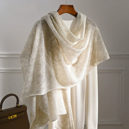 Ivory cashmere scarf with a subtle tonal pattern draped over a cream knit top.