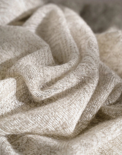 Close-up of ivory cashmere scarf fabric gathered into loose folds, showing its textured surface.