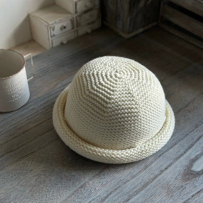 Ivory wool blend knit beanie with a rounded crown and rolled brim displayed on a wooden table