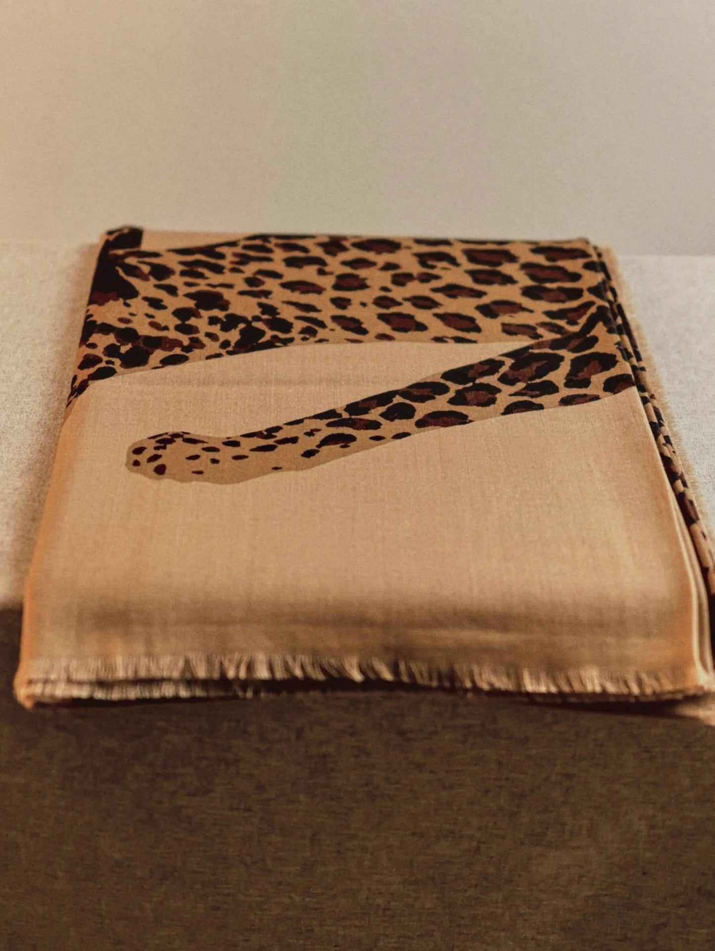 Folded khaki leopard print wool scarf showing its oversized animal graphic and soft neutral color