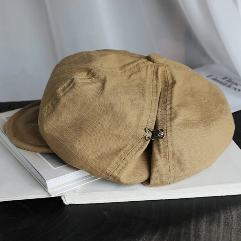 Khaki cotton beret hat displayed on a book, featuring breathable cotton fabric and adjustable elastic detail