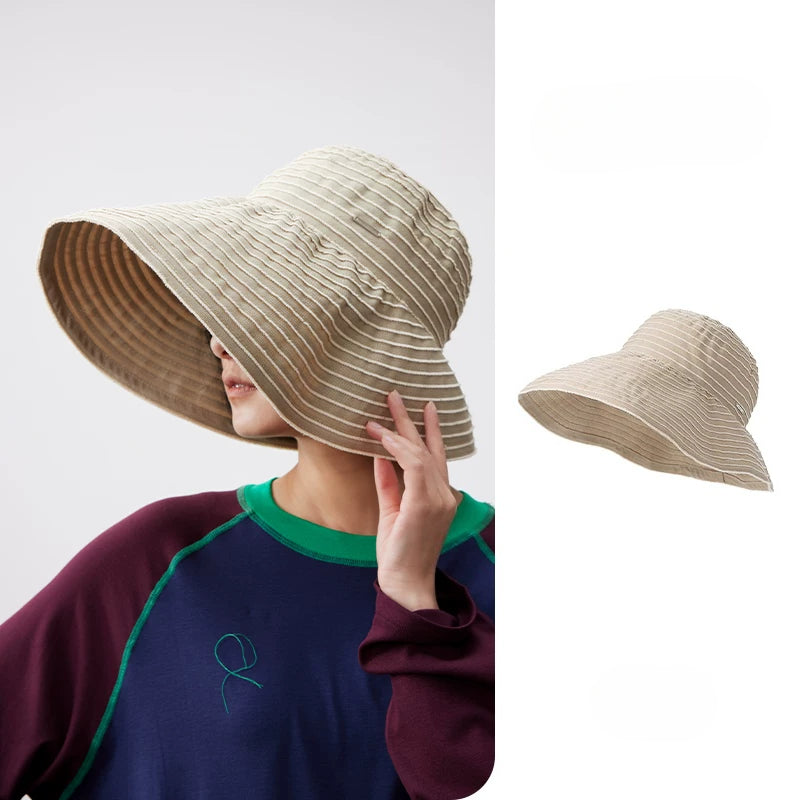 Woman wearing a khaki and white striped foldable wide brim sun hat with an adjustable chin strap.