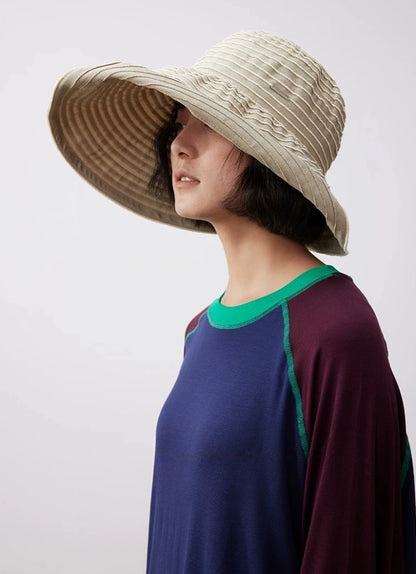 Side view of a khaki and white striped wide brim sun hat styled with a casual summer outfit.