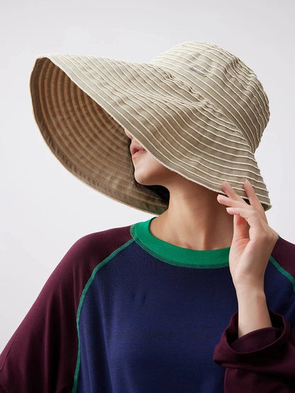 Woman adjusting a packable khaki striped sun hat with a soft curved brim for outdoor wear.