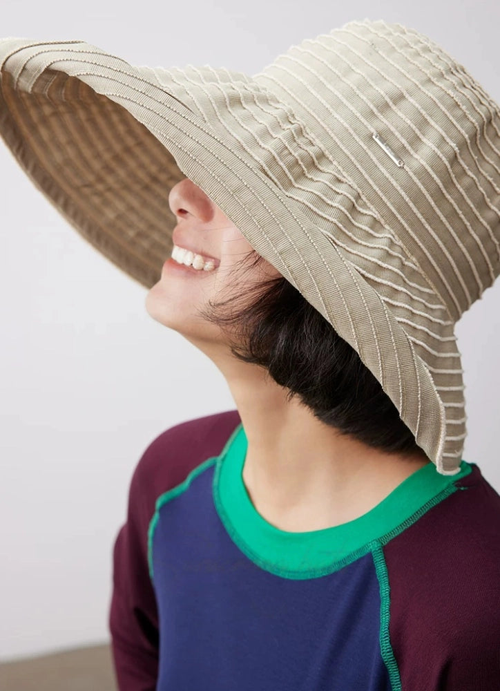 Close-up of a khaki and white foldable summer hat with a wide brim and lightweight striped design.