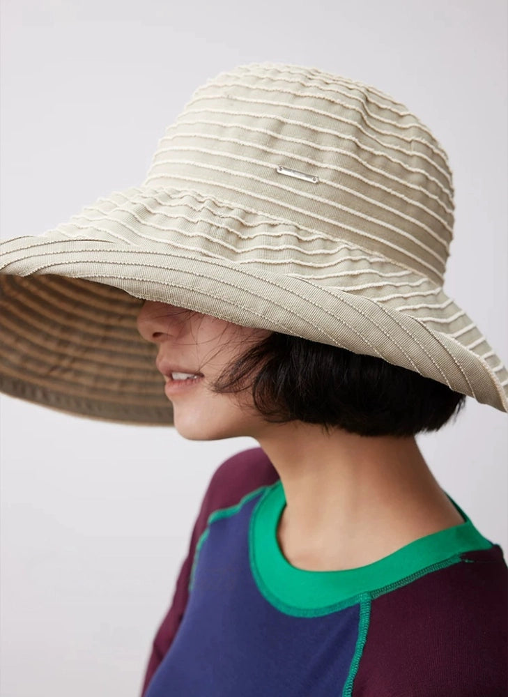 Woman wearing a khaki and white striped beach sun hat with a flexible brim for summer travel.