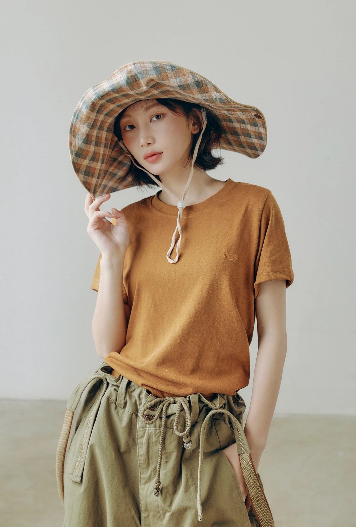 Plaid wide brim outdoor sun hat with string, worn with casual utility outfit for vintage cargo style.