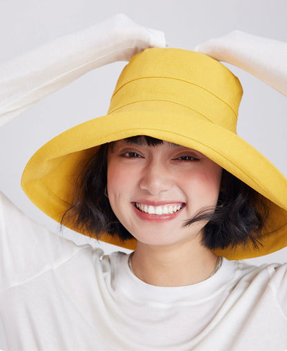Smiling woman adjusting a lemon yellow linen blend sun hat with a flexible full-coverage brim