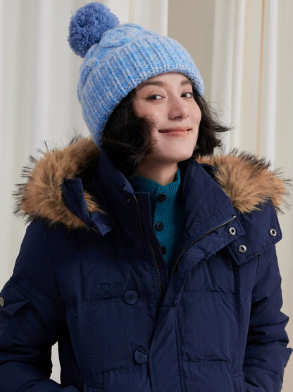 Model wearing a light blue cable knit pom pom beanie with a navy parka.