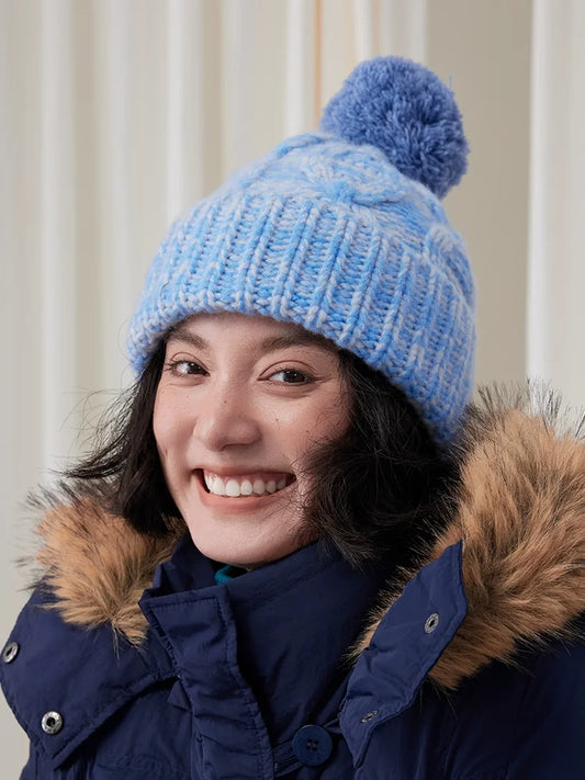 Front close-up of a light blue cable knit beanie with a matching blue pom pom and ribbed cuff.