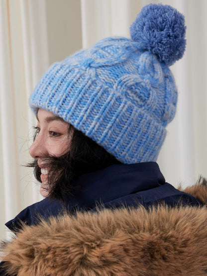 Side view of a light blue cable knit beanie, showing the blue pom pom and folded ribbed cuff.