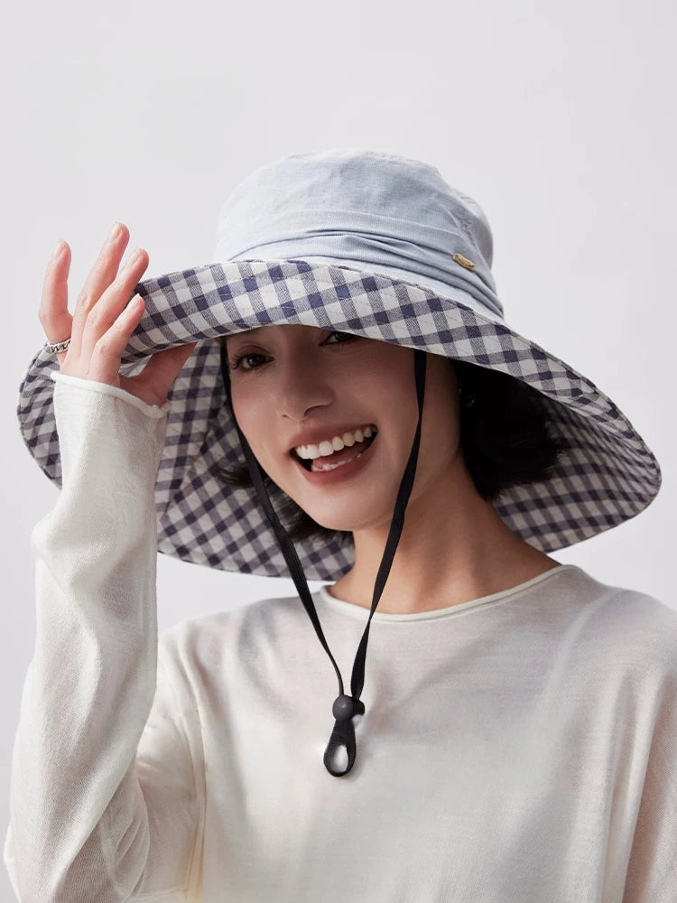 Smiling woman wearing light blue packable beach hat with plaid lining and adjustable wind cord