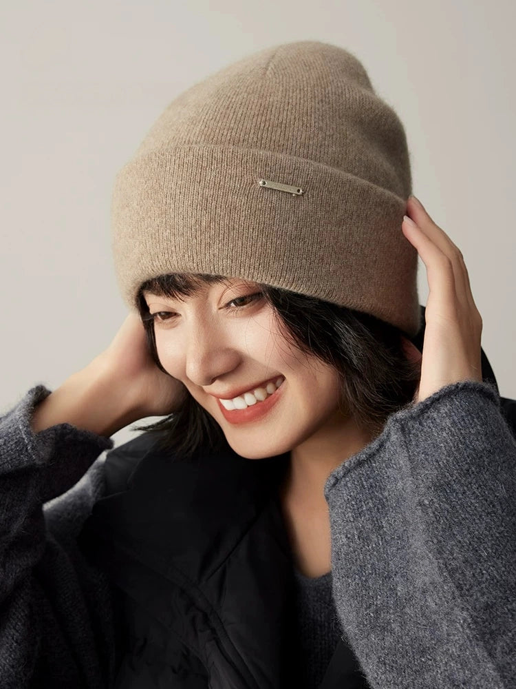Smiling woman adjusting a light coffee pure cashmere cuffed beanie for a cozy winter look