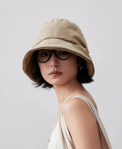 Front view of a light khaki pleated bucket hat styled with sunglasses for a casual outdoor look