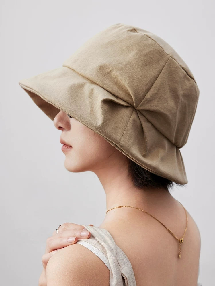 Profile view of a light khaki artistic pleated bucket hat with an asymmetrical folded brim
