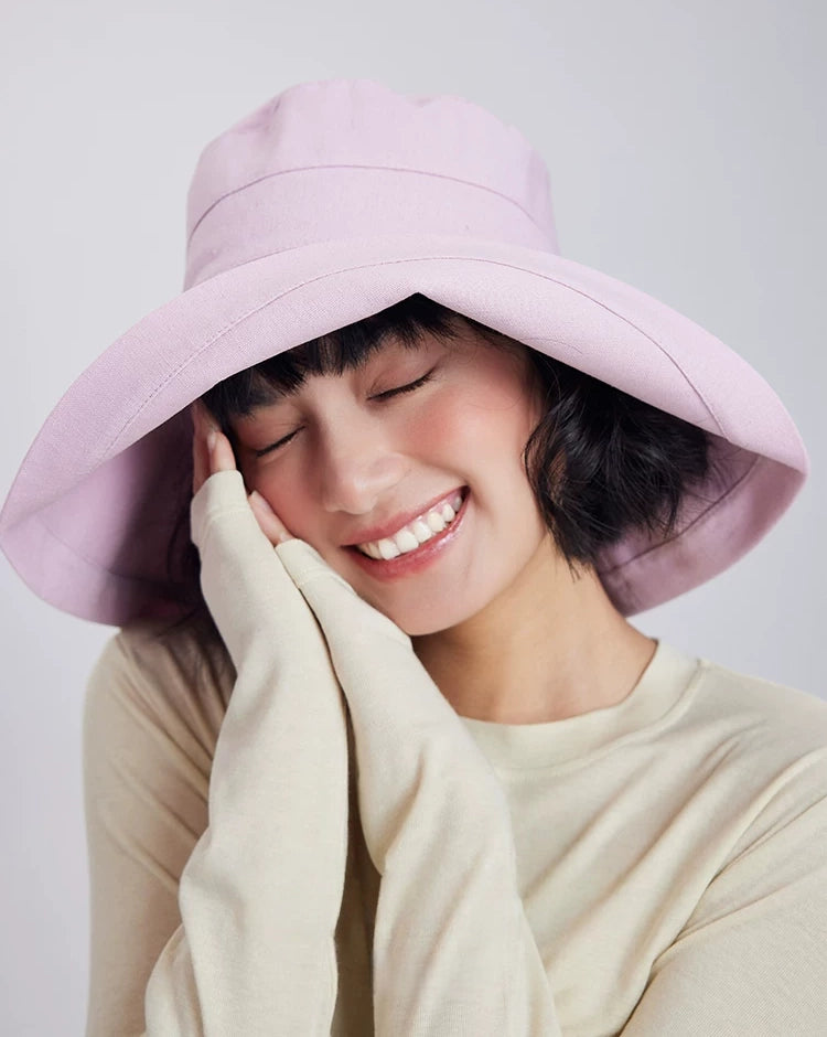Smiling woman wearing a light pink linen cotton sun hat with a gently curved wide brim
