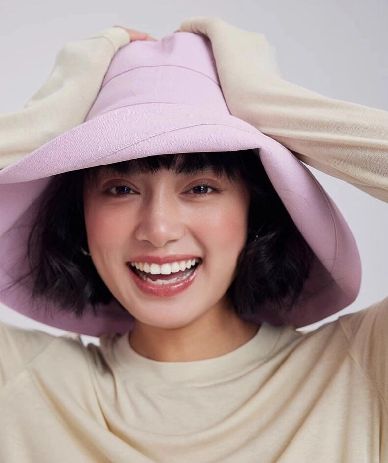 Woman adjusting a light pink packable sun hat with a flexible full-coverage brim