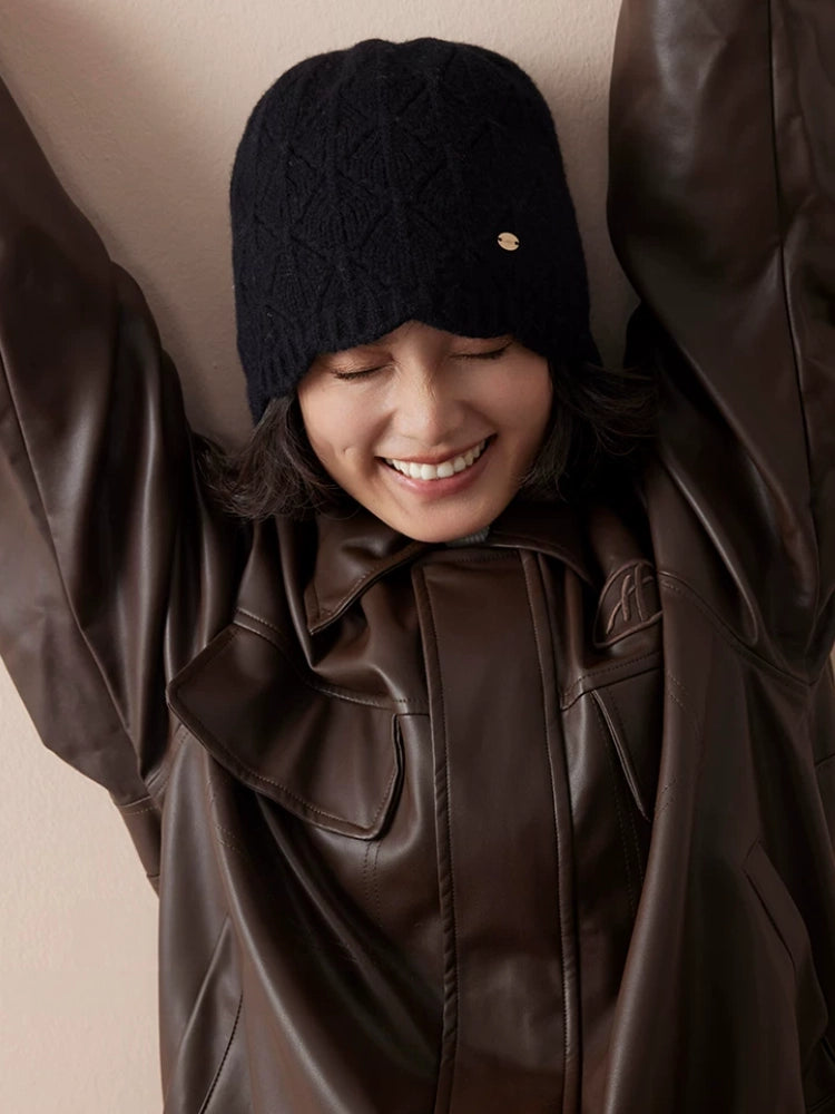Model wearing a black wool pointelle beanie low over the forehead with a brown leather jacket.