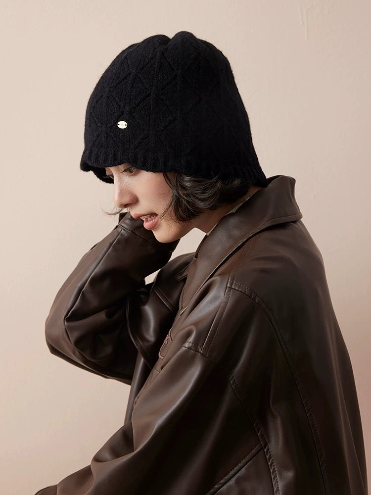 Side view of a black wool knit beanie with a relaxed crown, styled with a brown leather jacket.