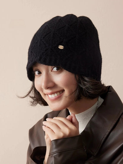 Model smiling in a black pointelle wool beanie with a small gold-tone badge.