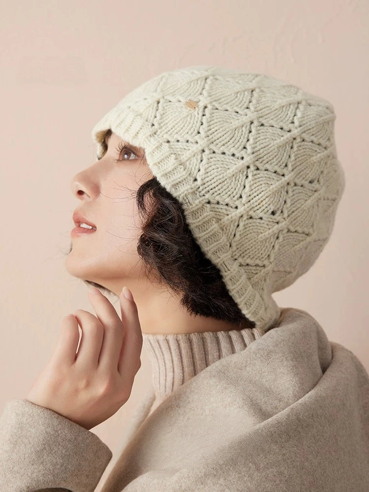 Side profile of a cream-white pointelle wool beanie, showing its close fit and rounded crown.
