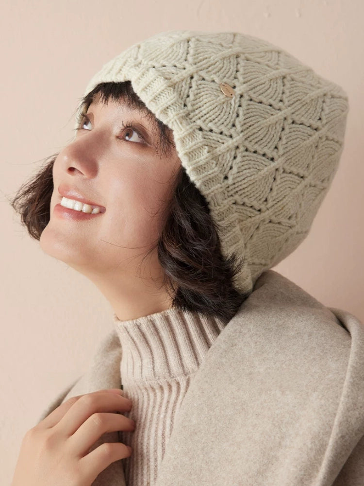 Close-up of a model looking upward in a cream-white wool pointelle beanie and beige outerwear.