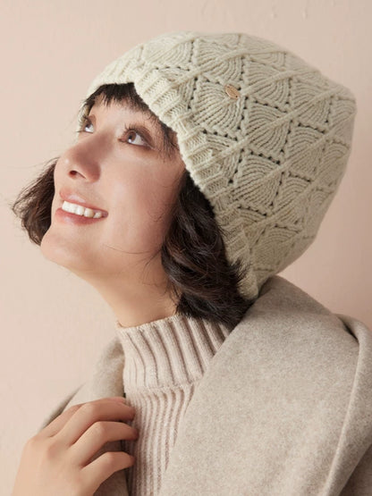 Close-up of a model looking upward in a cream-white wool pointelle beanie and beige outerwear.