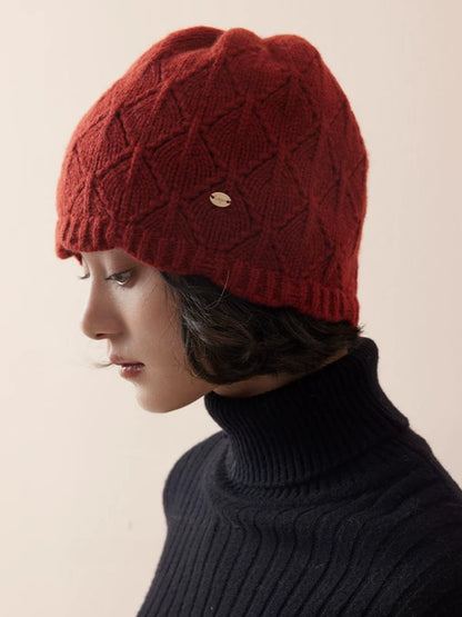 Side view of a red wool knit beanie showing raised diamond texture and a gold-tone badge.