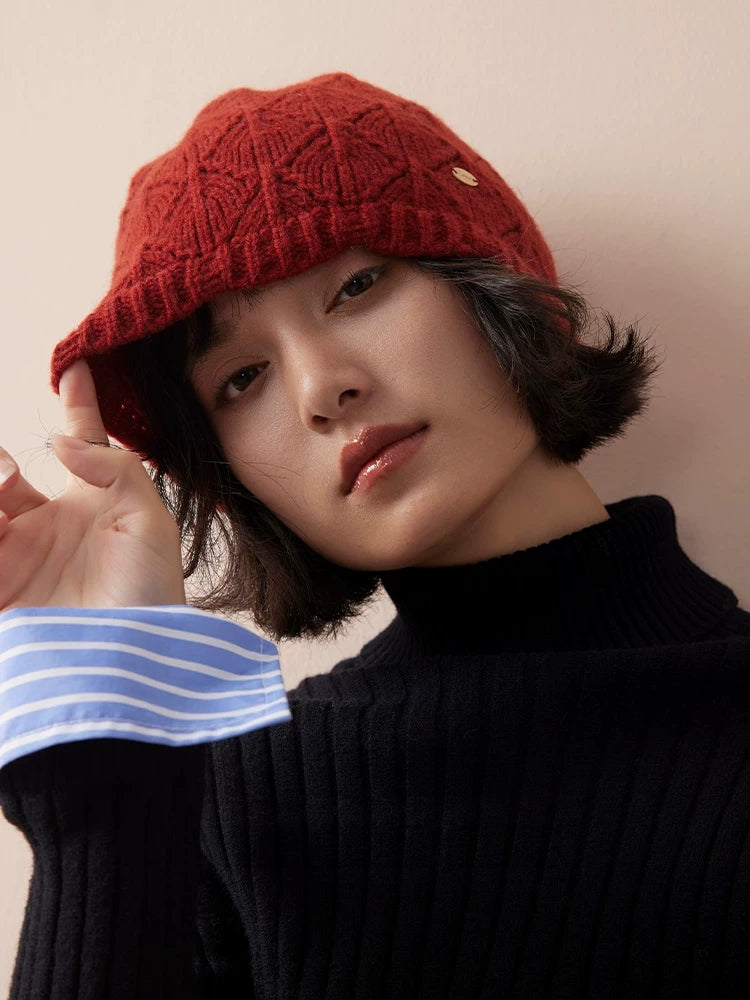Model touching the edge of a red wool pointelle beanie, with a black turtleneck and striped cuff.