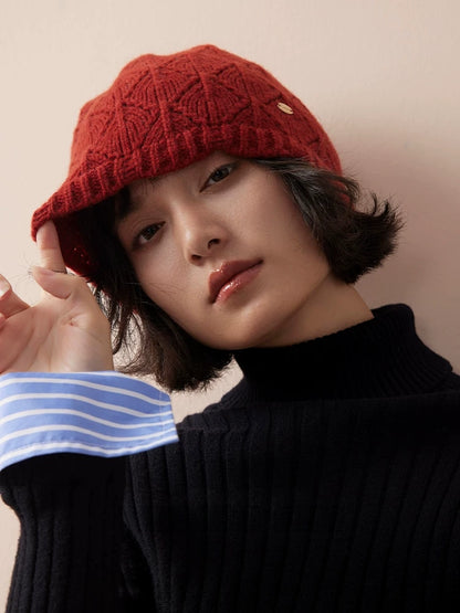 Model touching the edge of a red wool pointelle beanie, with a black turtleneck and striped cuff.