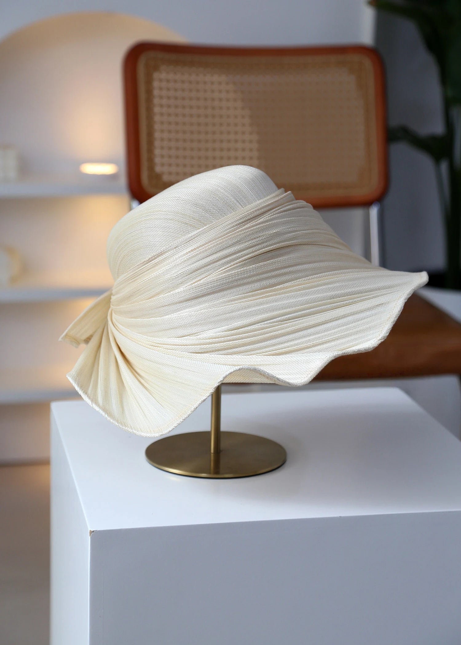 Ivory beige pleated straw hat on stand with lightweight Buntal straw weave.