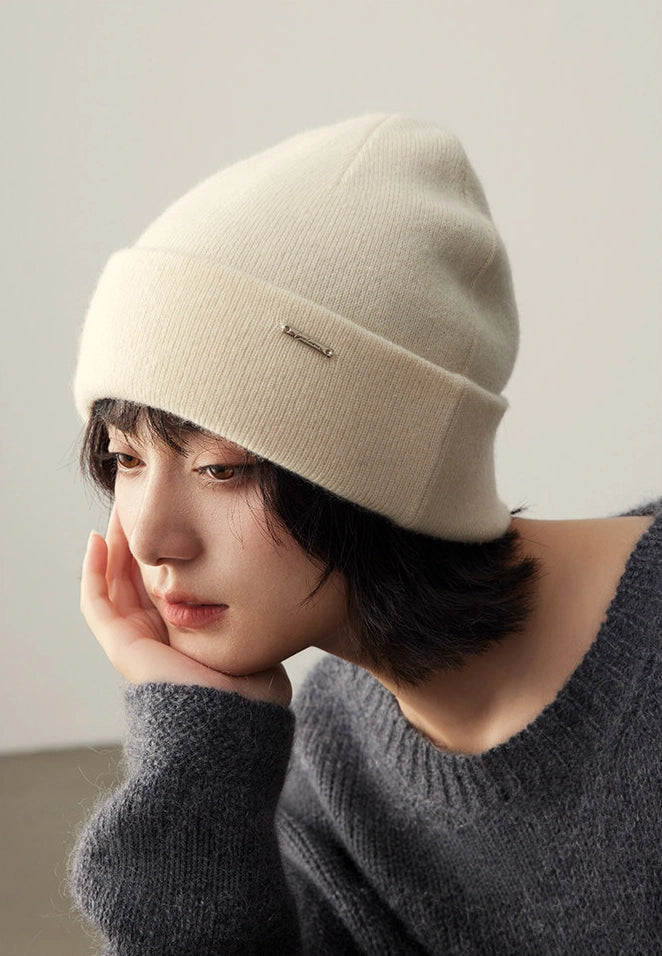 Close-up of a woman styling a milk white 100% cashmere cuffed beanie with winter knitwear