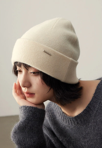 Close-up of a woman styling a milk white 100% cashmere cuffed beanie with winter knitwear