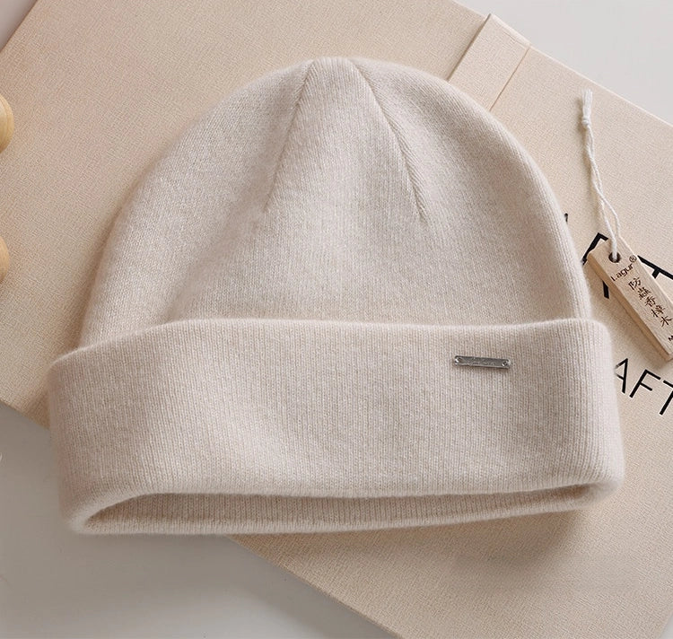 Milk white pure cashmere cuffed beanie with a small metal accent in a minimalist flat lay