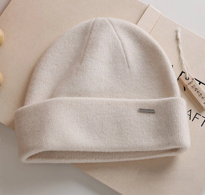 Milk white pure cashmere cuffed beanie with a small metal accent in a minimalist flat lay