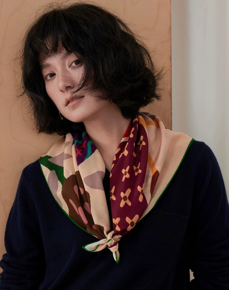 Woman wearing a cream graphic butterfly mulberry silk scarf loosely knotted over a navy top
