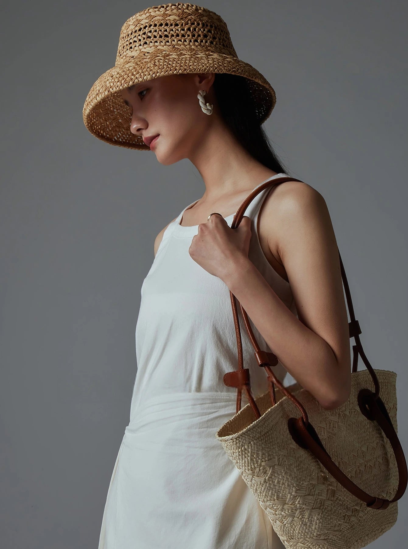 Woman wearing a natural raffia sun hat with a white summer dress and woven bag