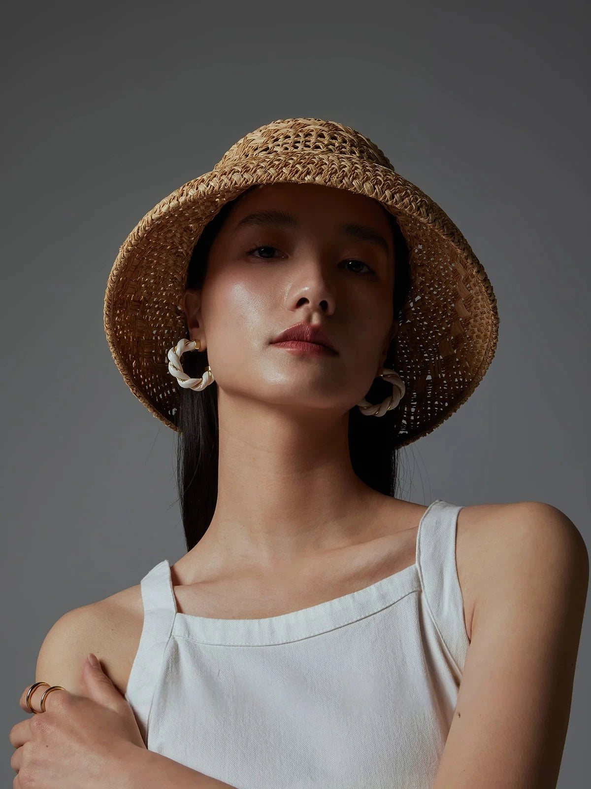 Front view of woman wearing a wide-brim raffia sun hat with a white top