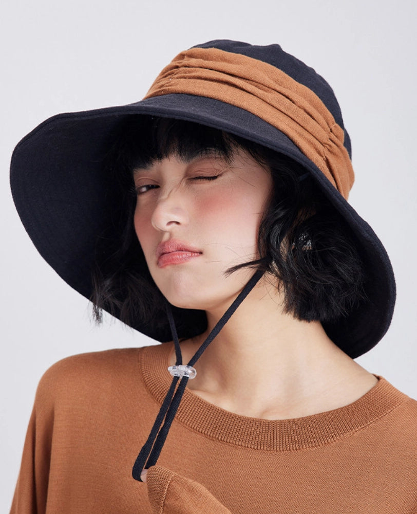Black brown wide brim bucket hat with wind cord, styled for beach travel and casual summer wear.