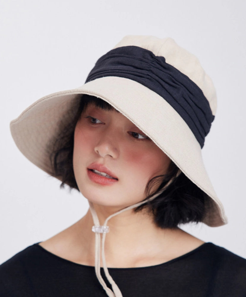 Model wearing an ivory beige ramie wide brim sun hat with black contrast band and adjustable wind cord.
