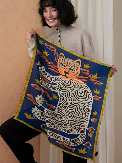 Woman holding an open navy blue mulberry silk scarf with orange and ivory leopards and a gold border
